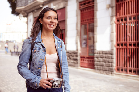 Pretty young girl walking down a narrow street with a camera wearing her long hair loose and casual...