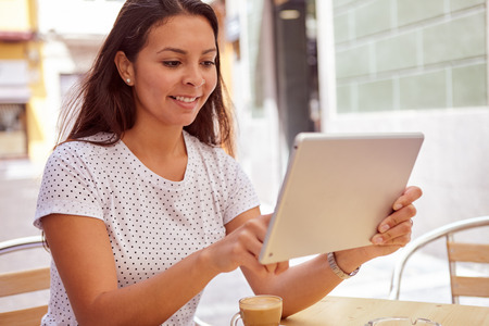 Cute happy young girl pointing at her tablet in a street cafe, relaxing while wearing her hair loose and casual clothingの写真素材