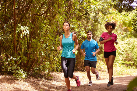 A young guy and two girls jogging on a gravel running trail with trees behind them while wearing t-shirts and black pantsの写真素材