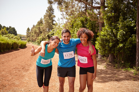 Three runners celebrating the end of a cross country marathon with trees behind them wearing casual running clothes in the late morningの写真素材