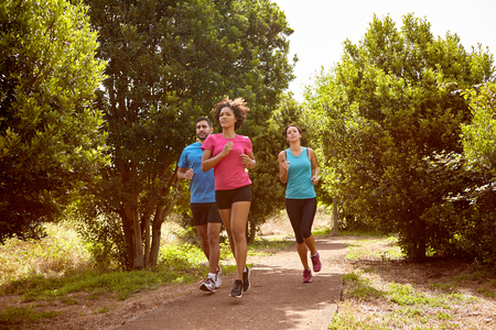 Group of three youngsters running through a natural trail in daylight surrounded by trees and bushes in the late morning wearing t-shirts and black pantsの写真素材