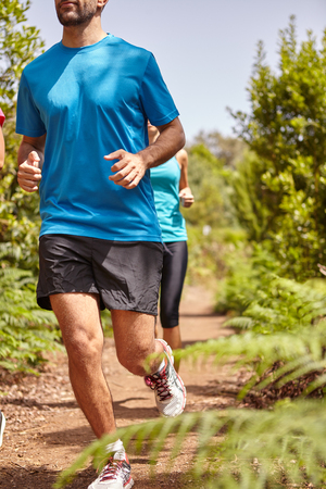 Two young joggers out for a run on a gravel path surrounded by bushes, wearing casual running clothes in the late morning sunの写真素材