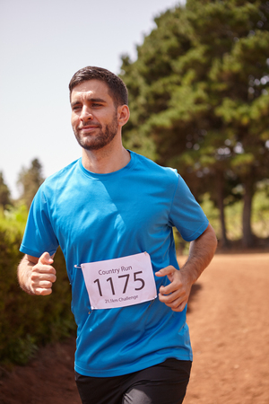 A young male running a cross country race with trees behind him wearing casual running clothes in the late morning sunの写真素材