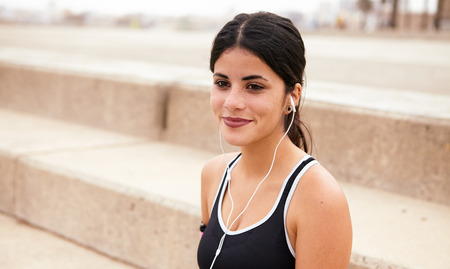Young brunette with earphones smiling dreamily with steps behind her while wearing casual clothes and looking aheadの写真素材