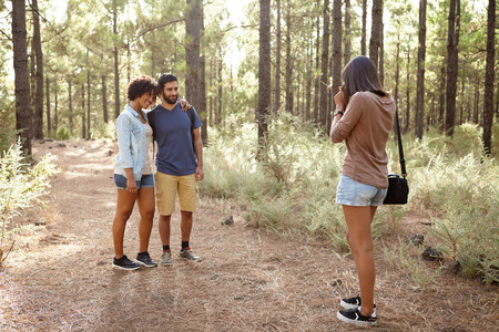 Three friends taking pictures of each other in a pine forest in the late afternoon sunshine, looking...