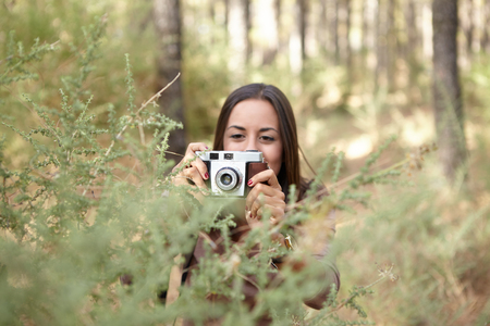 A young brunette taking a picture of a young sapling in a pine forest in the dappled late afternoon sunshineの写真素材