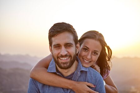 Happy young couple posing for a picture with a hazy mountainous background and happy smiles while wearing casual clothingの写真素材
