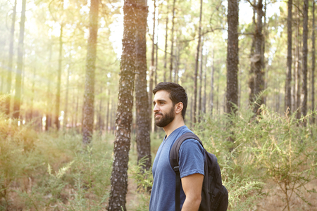 Young guy standing and listening to wind in the pine trees of a forest while wearing casual clothingの写真素材