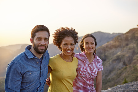 Young friends posing for a picture in the late afternoon sunshine with mountains behind them while wearing casual clothingの写真素材
