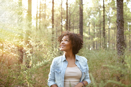 Young girl looking up and listening to the pine trees in a forest in the late afternoon sun while wearing casual clothingの写真素材