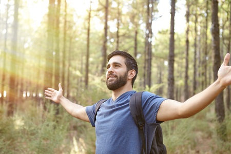 Young man feeling the energy of the forest with open arms in a plantation while wearing casual clothing and a backpackの写真素材
