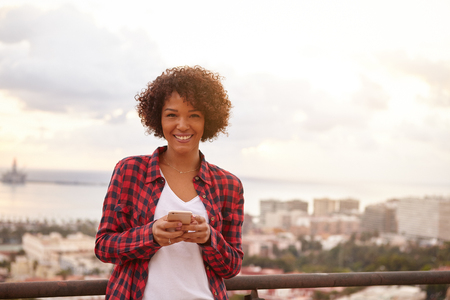 Young girl with a toothy smile looking at the camera, wearing a t-shirt and red and black shirt with a cityscape behind herの写真素材