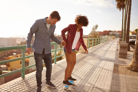Young man teaching girl to skateboard while holding her hand tightly in great concentration while she looks down at her feetの写真素材