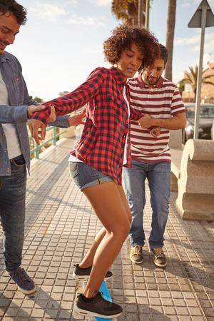 Two friends trying to teach a girl balance on a skateboard, the men holding the girl from either side, with great concentrationの写真素材