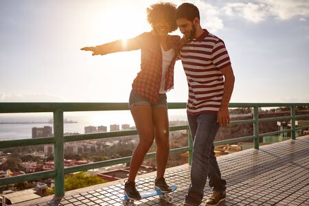 Boy showing girl how to skateboard while holding her up and her other arm straight out to keep her balance with bent kneesの写真素材
