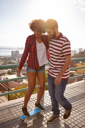 Boy showing girl how to skateboard while holding her up and walking her slowly while she leans on himの写真素材