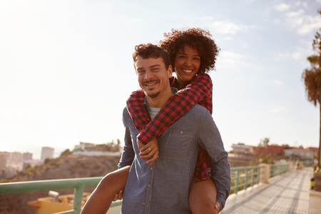 Joyful young girl getting a piggy back as she smiles a toothy smile with her arms around his neck while looking at the cameraの写真素材