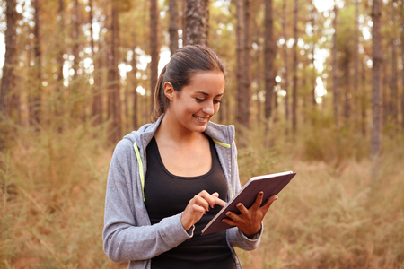 Smiling young girl concentrating on her tablet while holding it with her left hand and using her right index finger while in a forestの写真素材