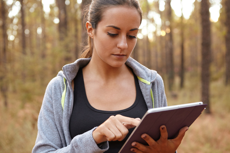 Cute young girl concentrating on her tablet while holding it with her left hand and using her right index finger while in a forestの写真素材
