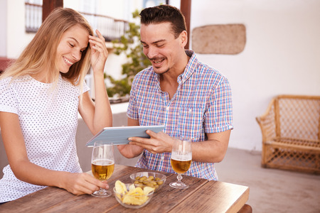 Good looking young couple looking at a tablet he is holding for her while she brushes her long blond hair out of her left eyeの写真素材