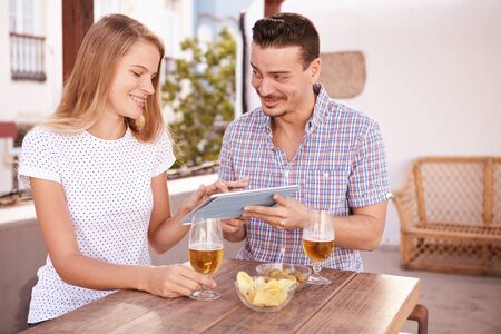 Beautiful young girl pointing at tablet handsome young man is holding for her while he is looking at her face with a smileの写真素材