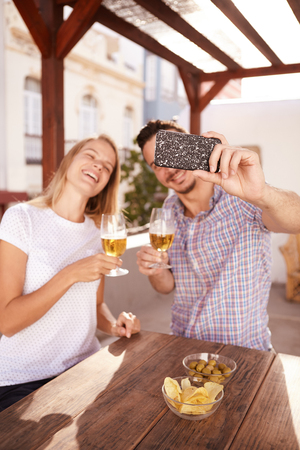 Happy couple with big smiles taking a selfie with their glasses raised to each other and her head thrown backの写真素材
