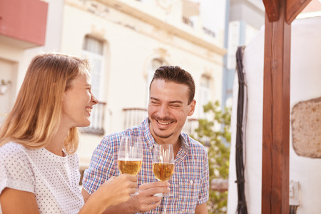 Cute couple laughing happily while they are enjoying some beers in the bright sunshine and all eyes on each otherの写真素材