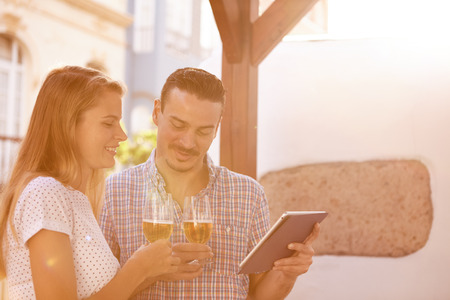 Young couple on a date looking at a touchpad while enjoying some beers and an intimate moment with bright sunshine directly behind themの写真素材