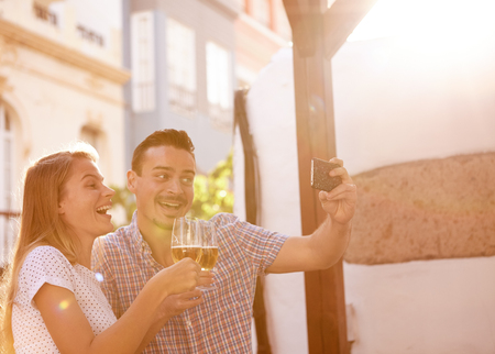 Couple taking a selfie while out for a few beers and laughing happily with the sun shining brightly behind themの写真素材