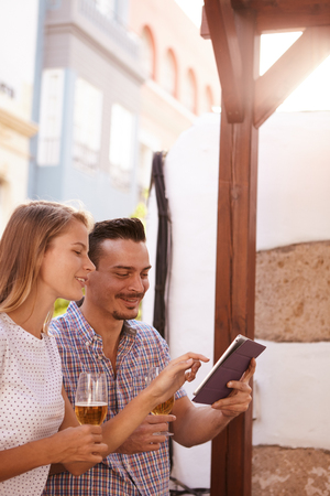 Young man holding tablet while his lovely girl is pointing at something on it as they are enjoying some beersの写真素材