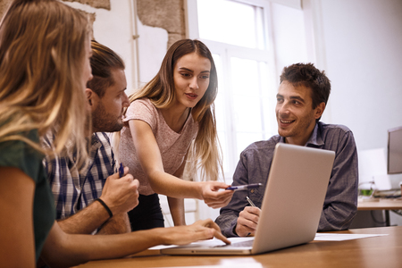 Professional young female presenter pointing to and explaining something on the laptop pc with enthusiasm to the rest of the team in a meetingの写真素材