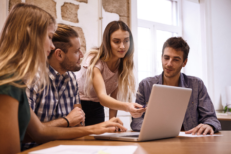 Four young business professionals in a captivating and energetic strategic meeting at a desk with a laptop pc and some notes on the tableの写真素材