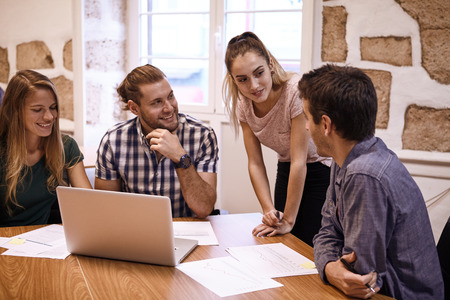 Professional young business team in a brainstorming session looking and listening to each others fresh new ideas all looking at one of the male participantsの写真素材