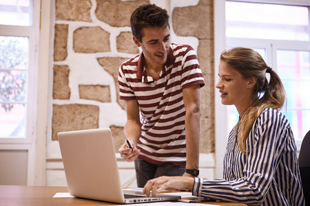 Professional young businesswoman showing a young man something on a laptop they are sharing while he is looking at her with a pen in handの写真素材