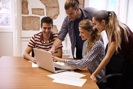 Young business team in a meeting with one male and one female both pointing at the laptop they are all sharing while everyone is smilingの写真素材