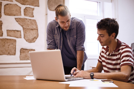 Young male business team working with deep concentration looking and pointing at the laptop screen with interestの写真素材