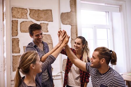 Four young people giving each other a high five with the girls looking at each other and all with...