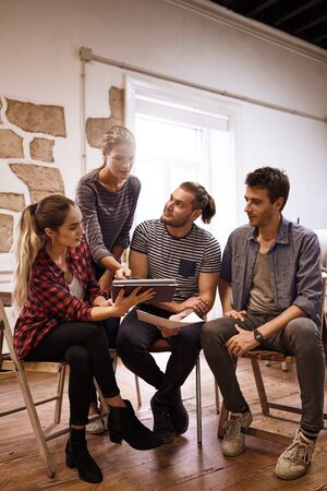 Motivated young business team in a meeting while one lady hands a tablet over to the other lady in the group of fourの写真素材