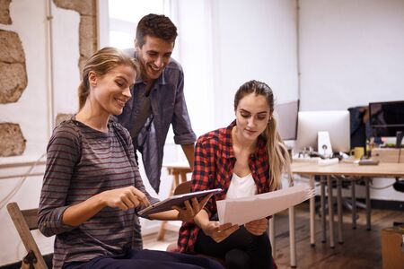 Team of three young business people looking very happy while one lady is pointing at something on the tablet she is holdingの写真素材
