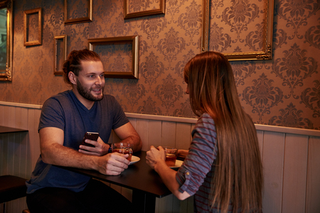 Happy young couple sitting at a small bar table talking and looking at each other while having some teaの写真素材