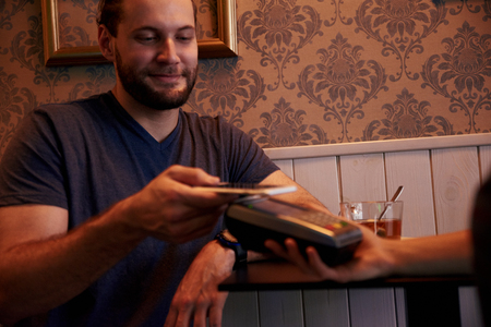 Young man offering his cell phone above the payment machine while looking at the the phone with a smileの写真素材