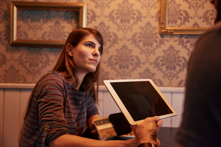 Young waiter types something on his tablet with credit card while a young woman is looking at him with interestの写真素材