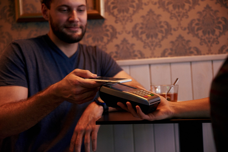 Handsome young man offering to pay his check with his cellphone held out above the payment device held by anotherの写真素材