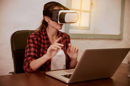 Cute young woman with a 3d viewer to her eyes sitting with her laptop in front of her while...