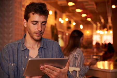 Thoughtfully Smiling Millennial Gay Sitting In Restaurant Texting