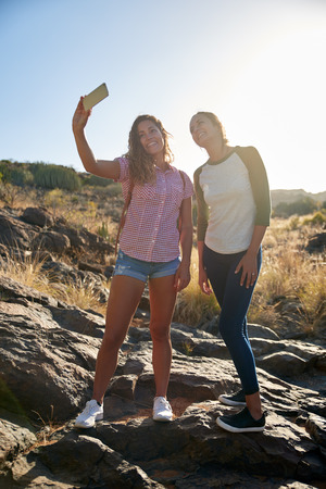 Two lovely young girls on a big rock posing for a selfie while wearing casual clothing in the afternoon sunshineの写真素材