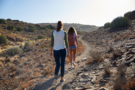 Two young girls wearing casual clothing with their long hair hanging loose strolling up a rocky hillside pathway in the sunshineの写真素材