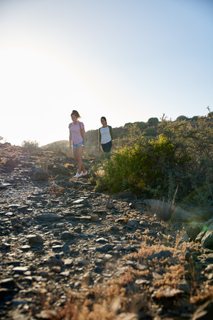 Concentrating girls hiking down a rocky mountain side wearing casual clothing and their arms beside them in bright reflective late afternoon sunの写真素材