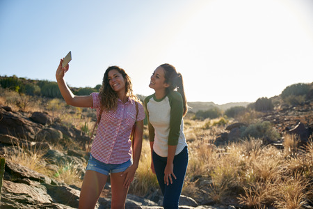 Two pretty young girls posing on a big rock for a selfie while wearing casual clothing in the afternoon sunshineの写真素材