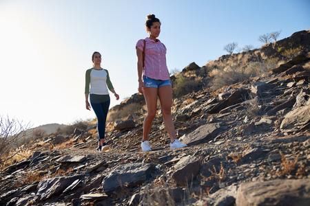 Two strong and healthy young ladies hiking on a rocky hillside wearing casual clothing with their arms beside them in the afternoon sunの写真素材